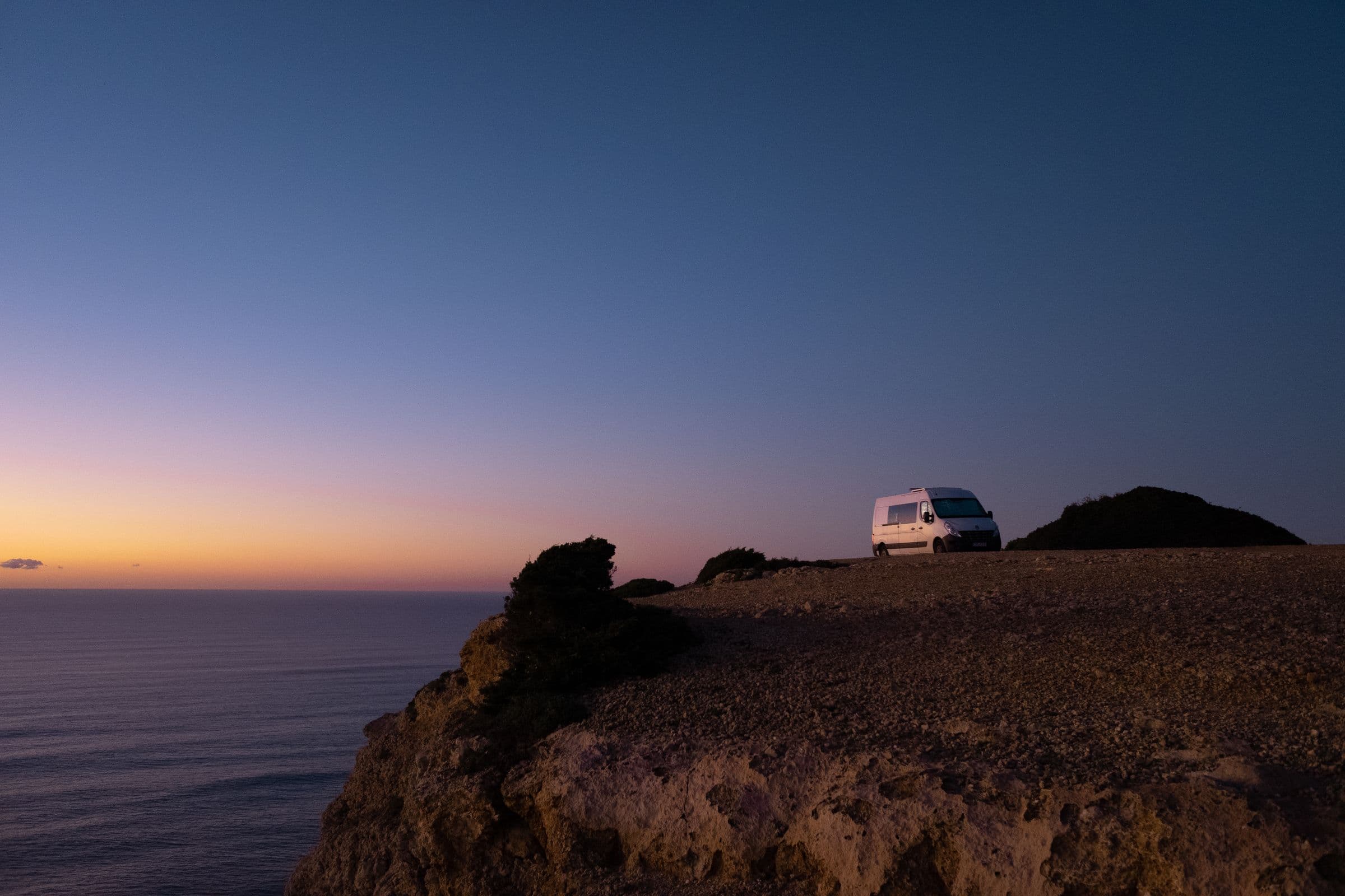 A campervan parked on a coastal bluff at sunset